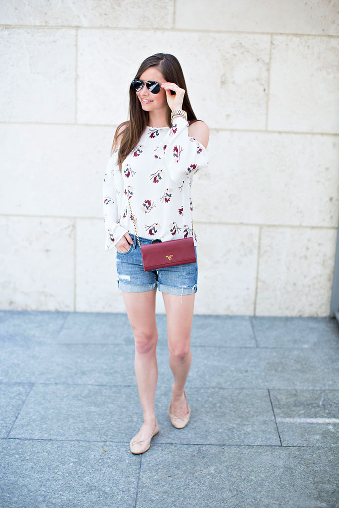 A fall transition style with a floral cold shoulder top, distressed boyfriend shorts, Prada wallet on a chain and classic ballet flats