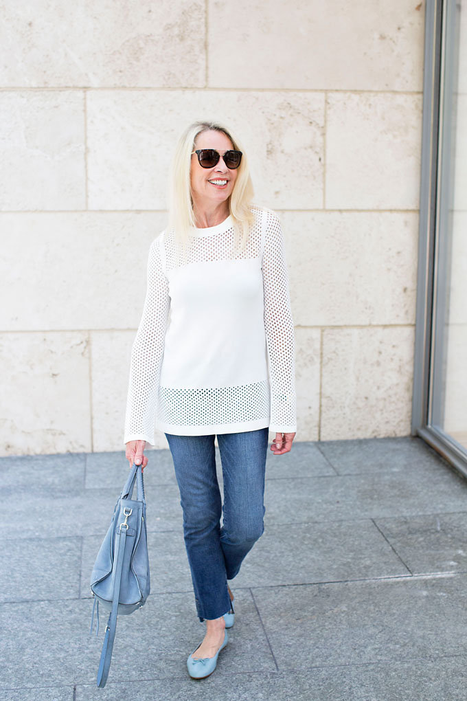 A winter white sweater with sheer sleeves and neckand hemline with jeans and a blue suede handbag and baby blue ballet flats