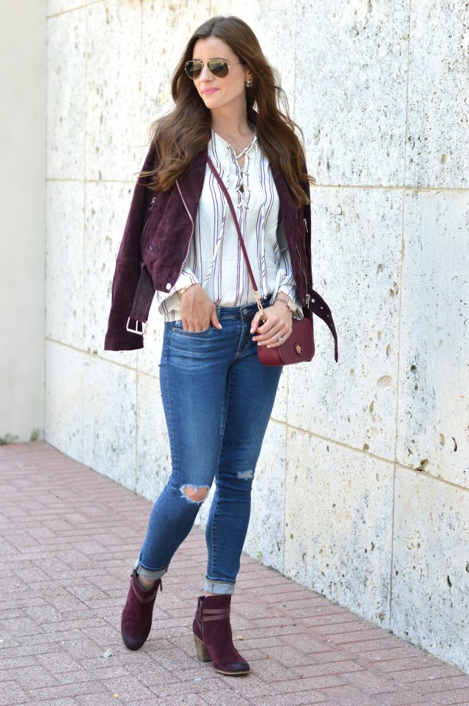 Burgundy suede moto jacket with a small cross body bag in oxblood and burgundy moto booties and distressed jeans.