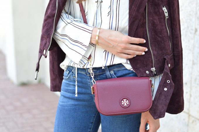 Burgundy suede moto jacket worn over a striped lace up top and carrying a burgundy cross body bag and Cartier Love bracelet.