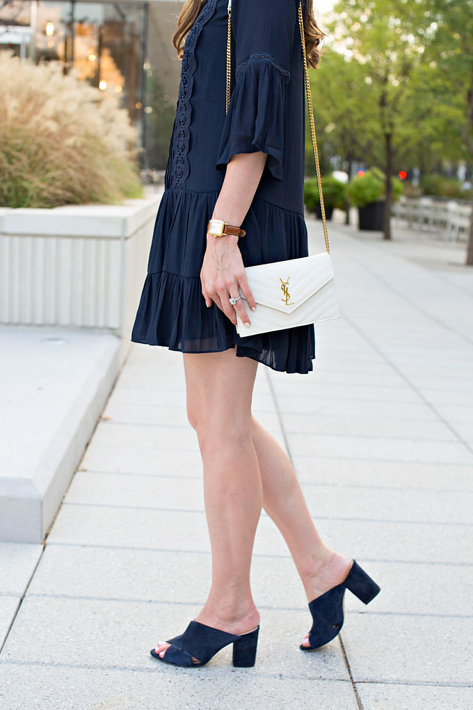 A blue shirtdress with flutter hem, worn with a white shoulder bag and blue suede mules.