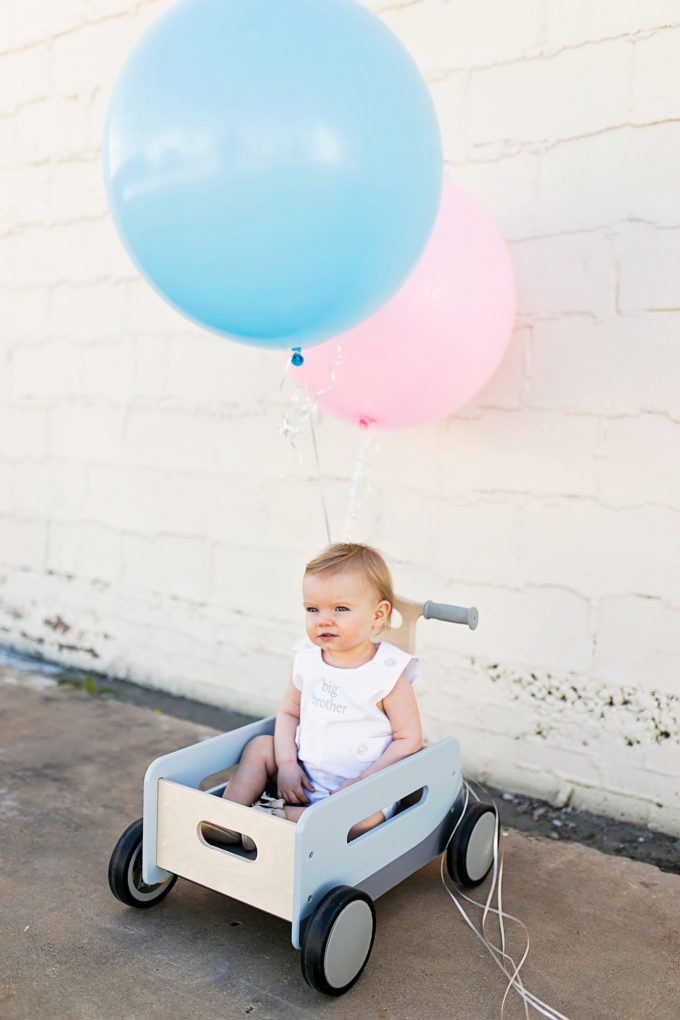 baby sitting in wagon with blue and pink balloons