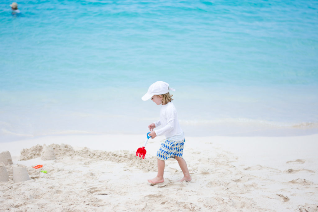 boy walking along beach with sand toys