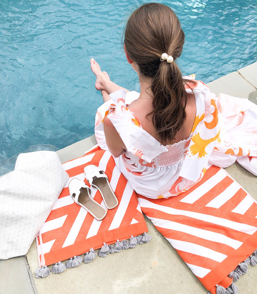 woman sitting by a pool orange white striped tassel towels