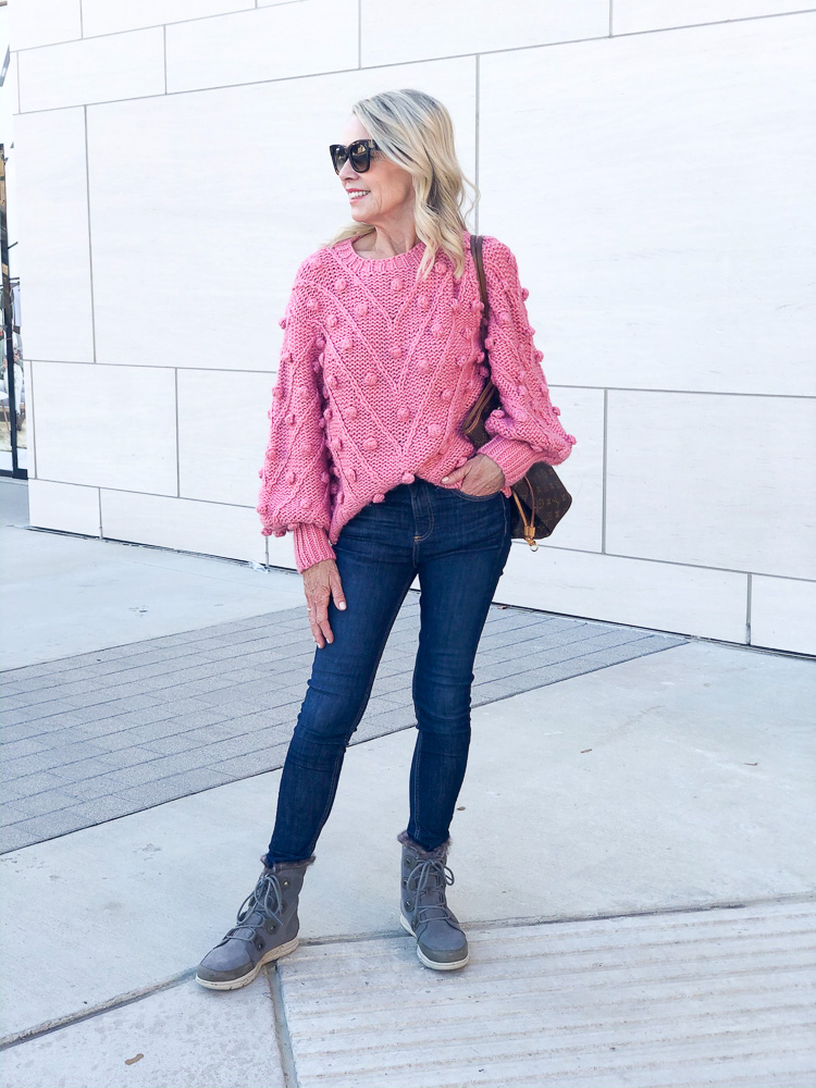 woman wearing pink pom pom sweater skinny jeans and boots