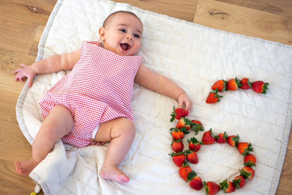 six month old baby next to strawberry six