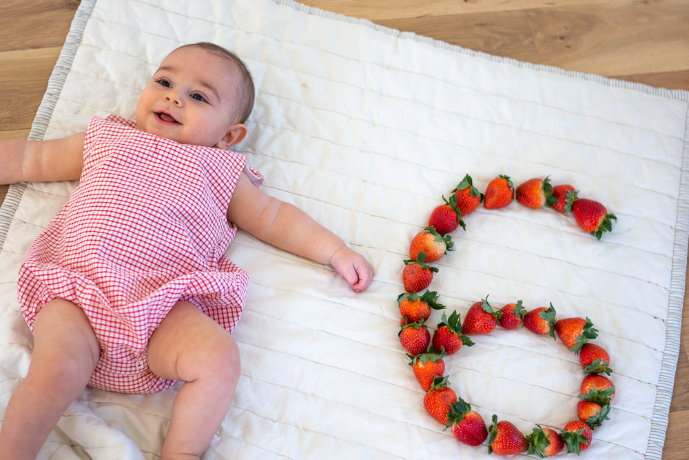 six month old baby next to a strawberry six