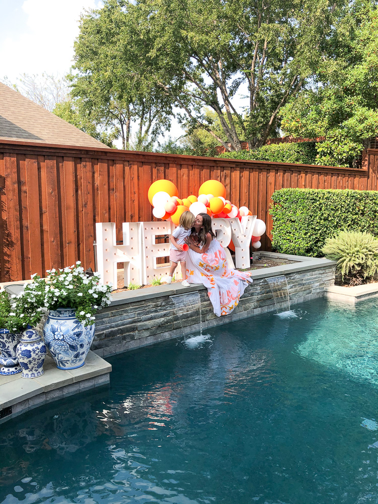 mom with toddler boy by pool with henry sign and balloons