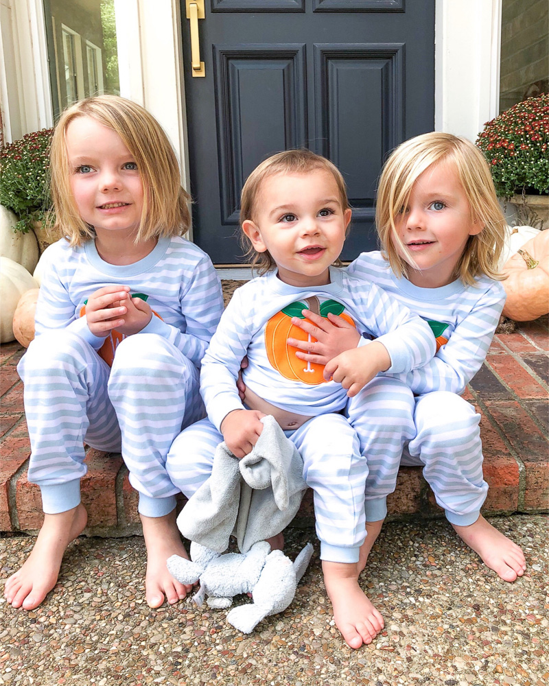 three toddler brothers sitting on front porch in pumpkin pajamas