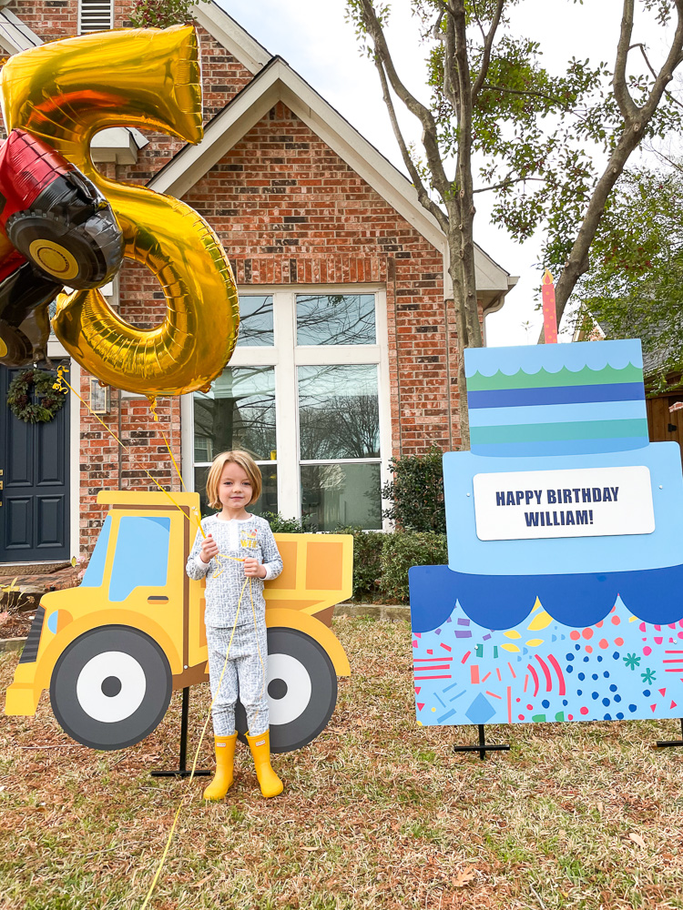 boy in ront yard with happy birthday sign an 5 balloon