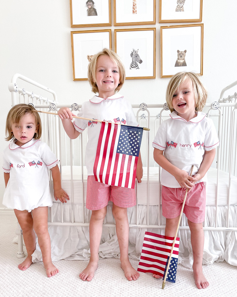 three toddler brothers holding American flags by crib