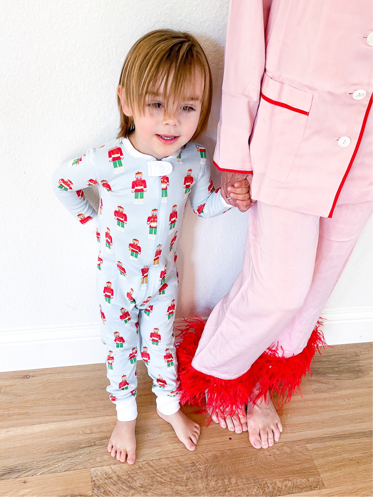 toddler boy in christmas pajamas holding hands with woman in pink pajama set with feather hem
