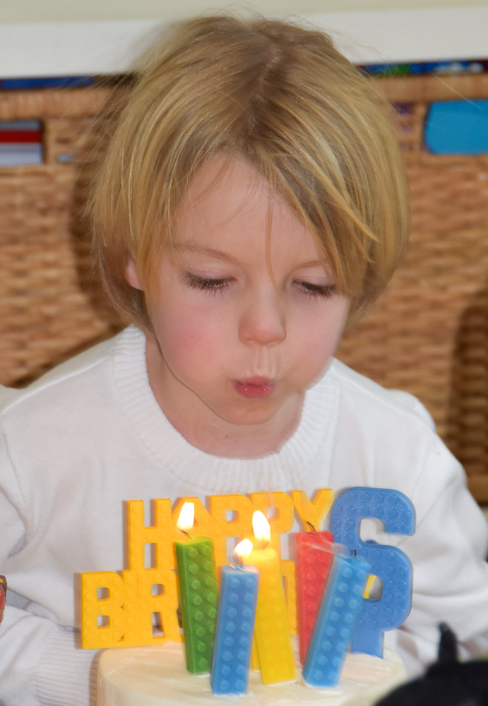 boy blowing out lego themed birthday candles