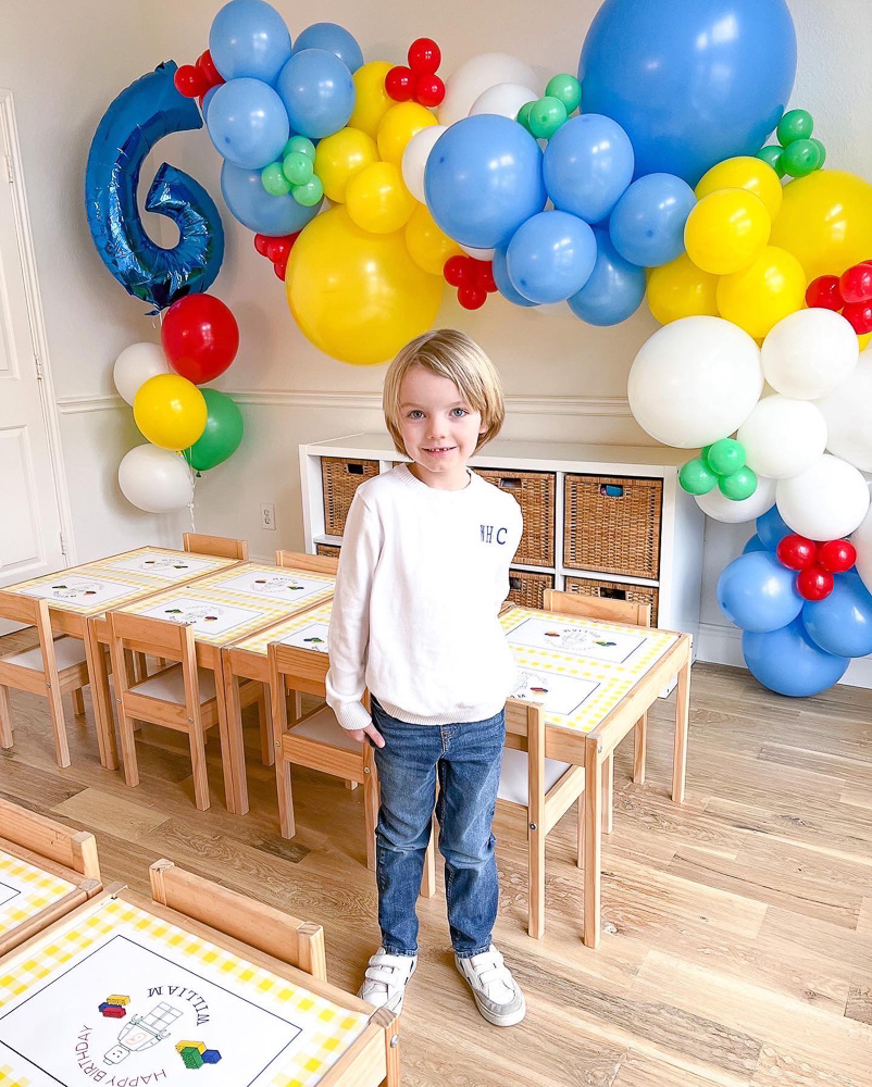 boy standing in party room with balloon garland and number six