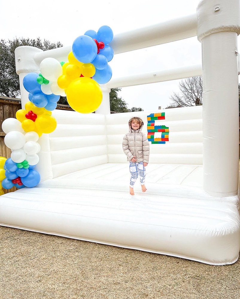 boy standing in white bounce house with colorful ballon garland and number six decal