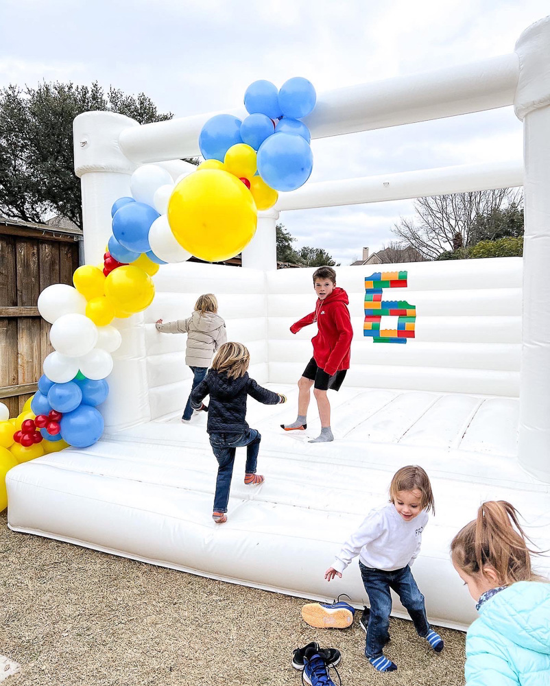 kids playing in white bounce house with colorful balloon garland and number six decal