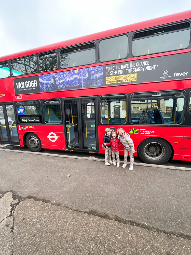 three little boys standing in front of red double decker bus in london