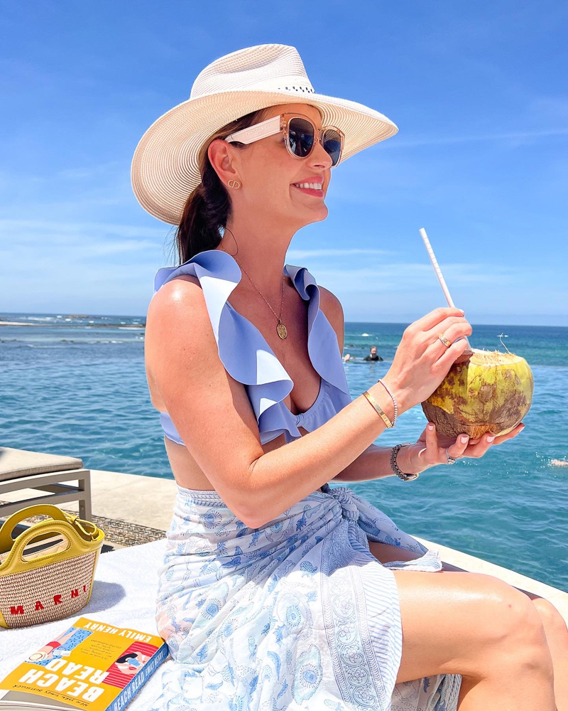 woman in white hat holding a coconut cocktail poolside