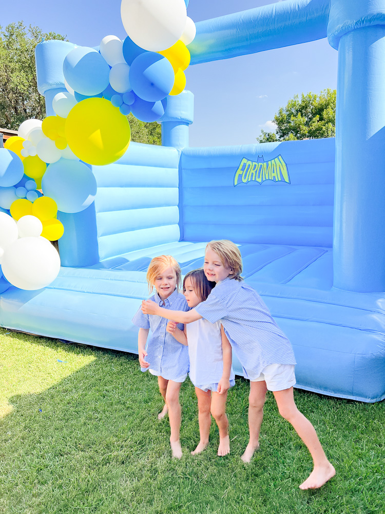 three brothers posing in front of blue bounce house with balloon garland