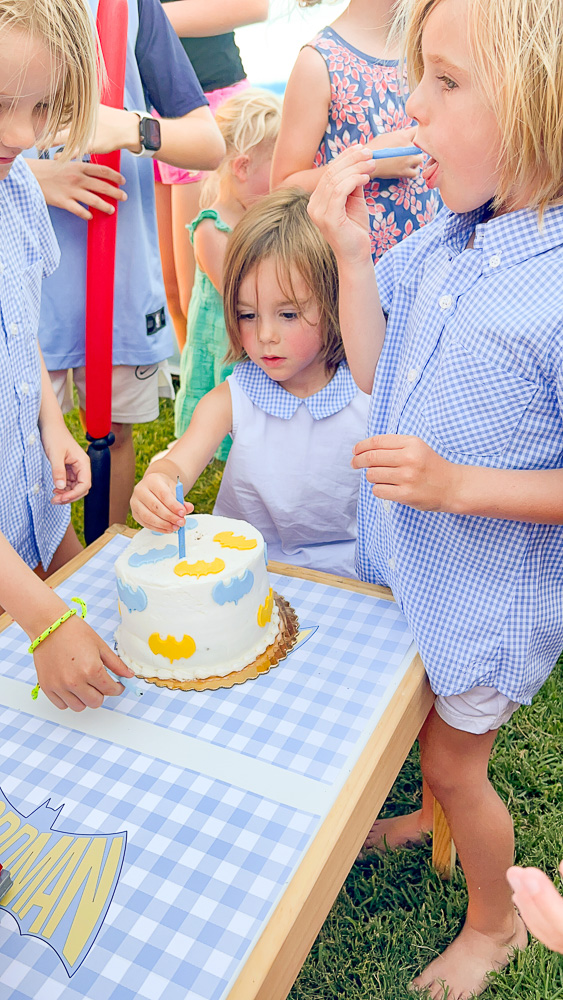toddler boy sitting in front of birthday cake with children around him