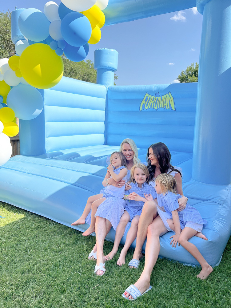 two women sitting on edge of bounce house with three little boys