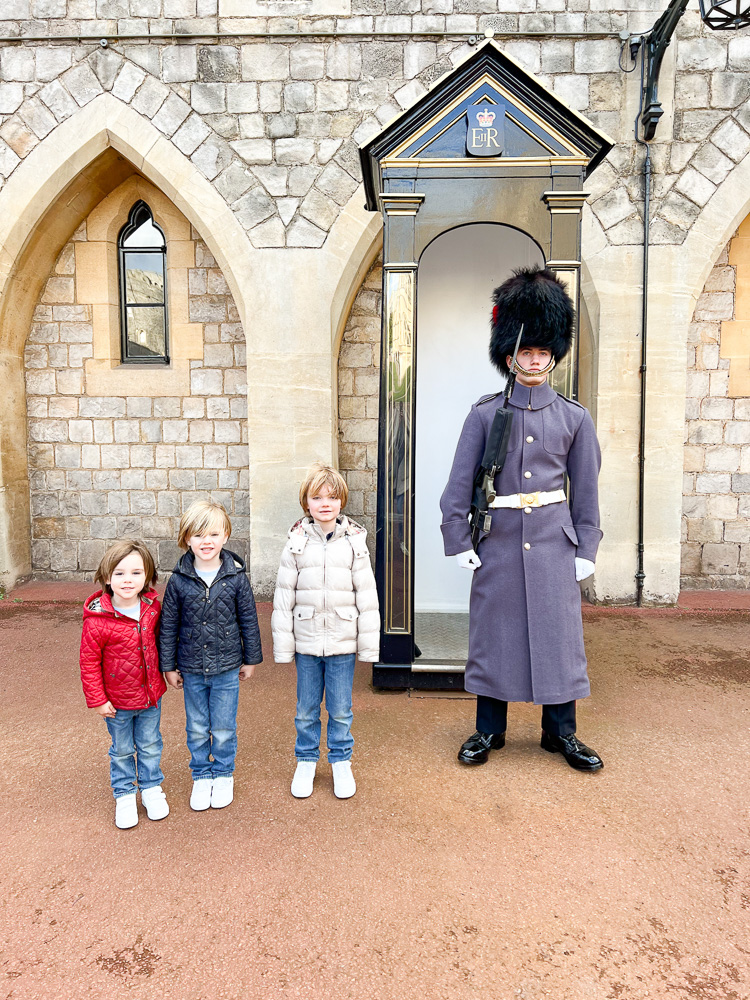 three little boys standing next to royal guard at windsor castle