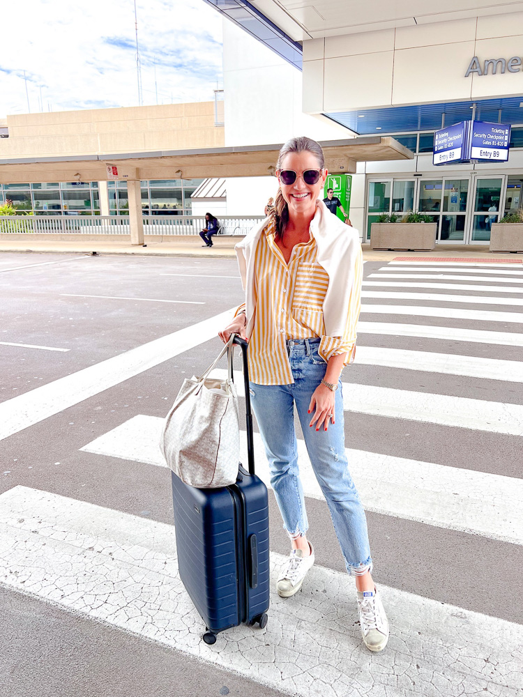 woman standing outside airport in yellow striped shirt with suitcase