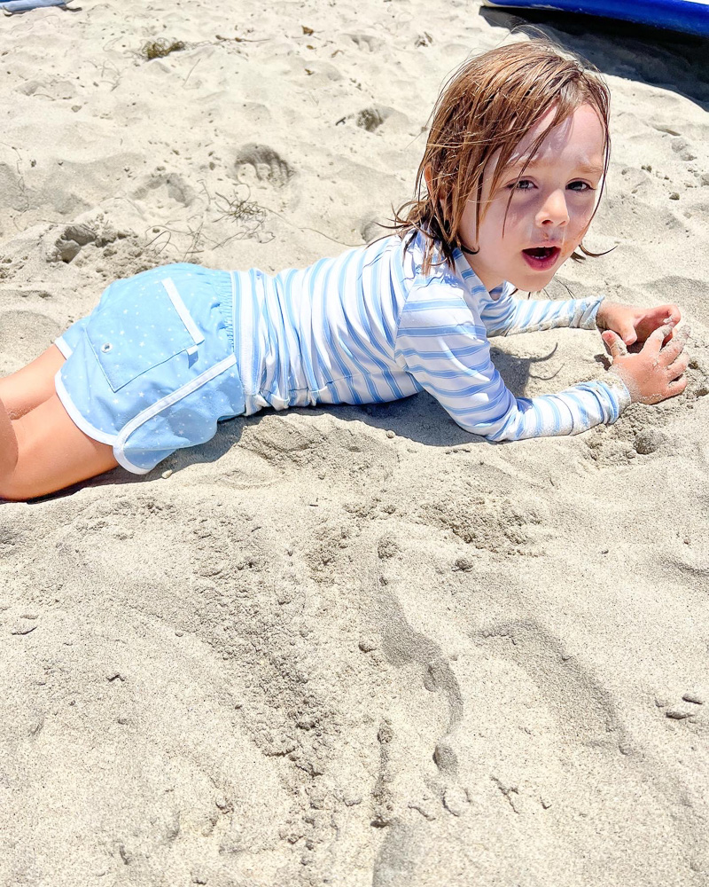 toddler boy laying in the sand at the beach