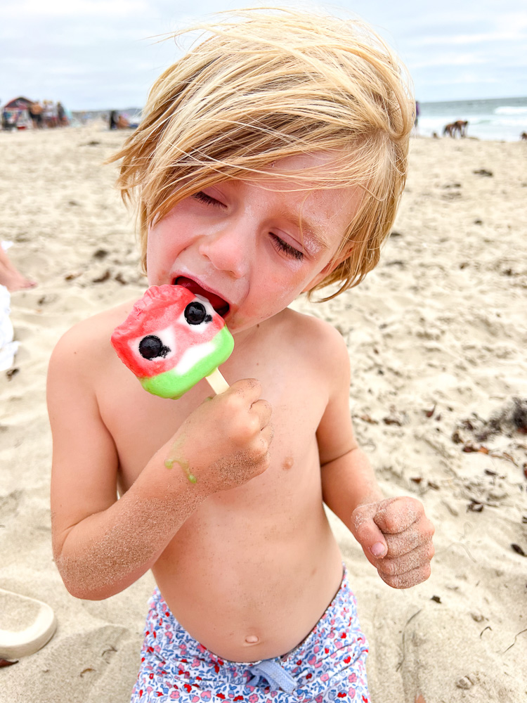 little boy eating popsicle at the beach