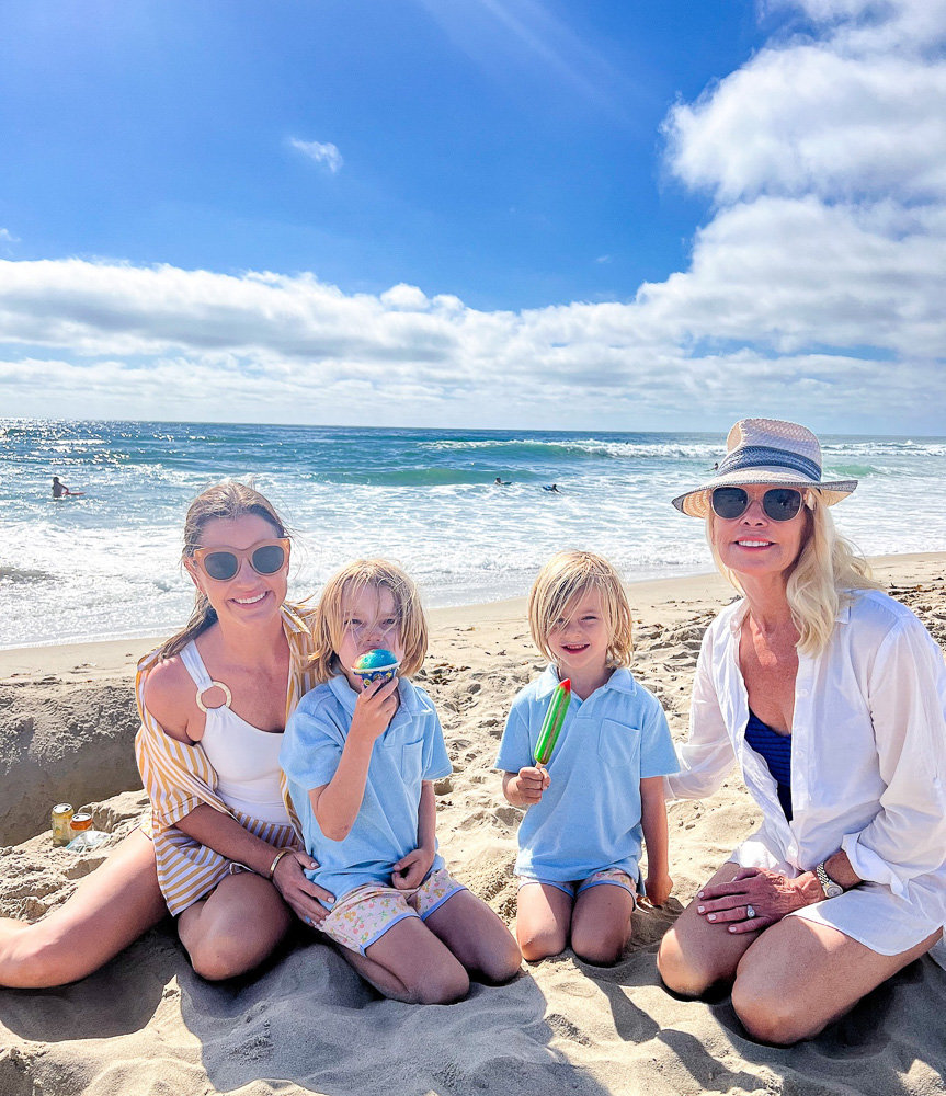 two women sitting on the sand with two little boys eating popsicles at the beach