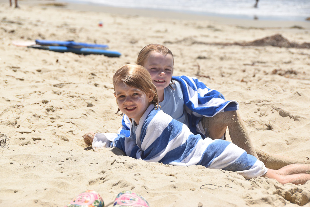 two little boys laying in the sand at the beach