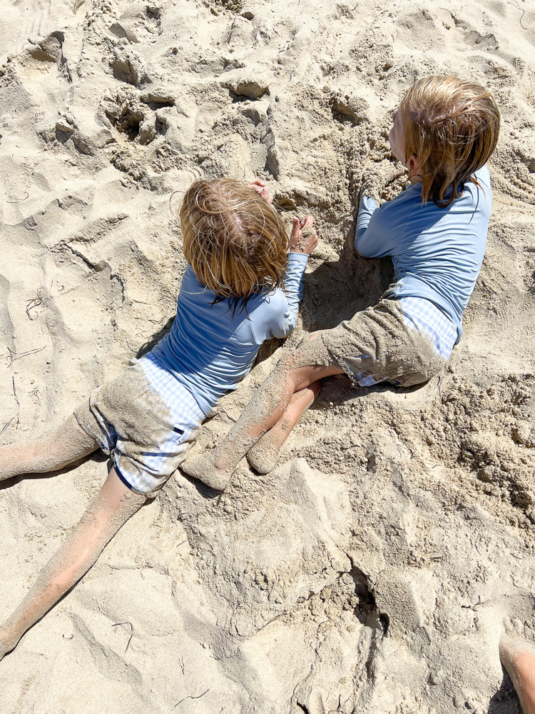 two little boys laying in the sand at the beach