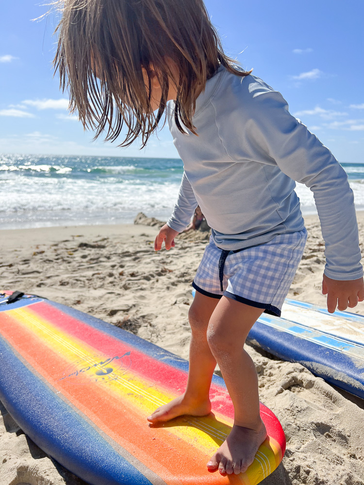 little boy standing on boogie board at the beach