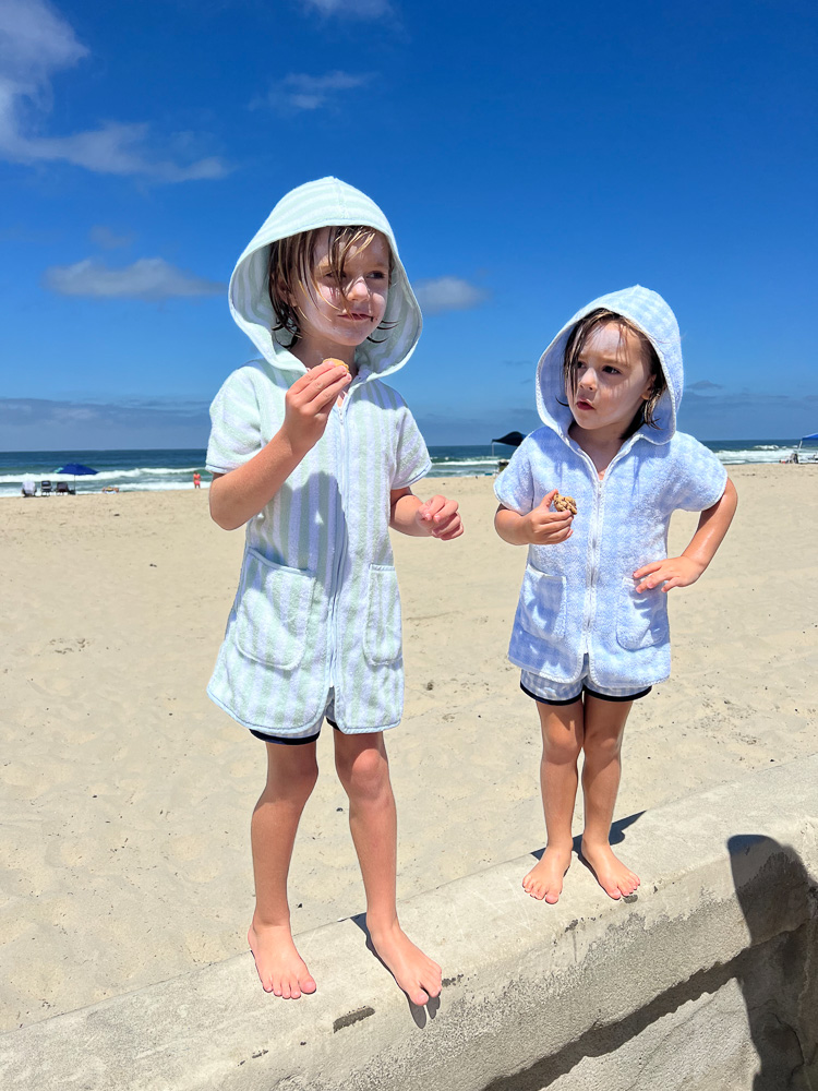 two boys in hooded towel robes standing on sea wall