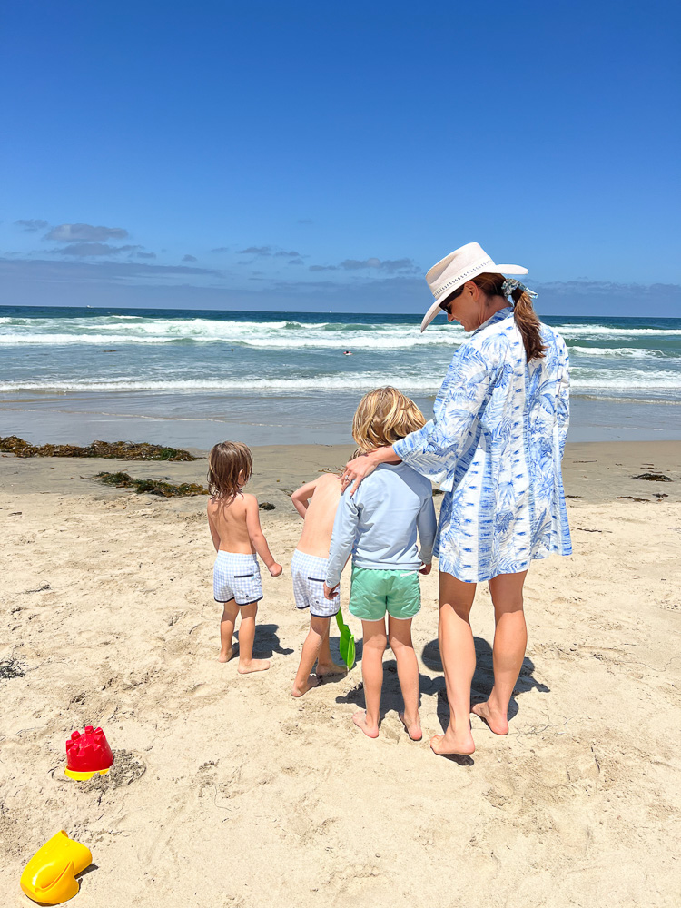 mom in cover-up and hat with three little boys at the beach