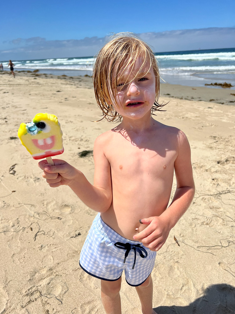 little boy standing on the beach eating a popsicle