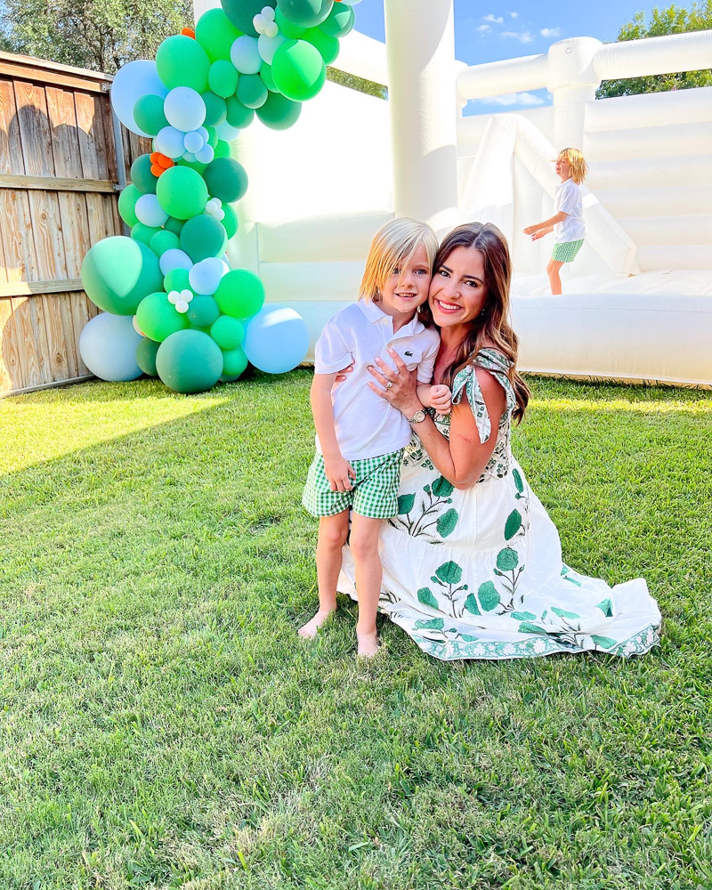 mom with little boy in front of bounce house with green balloon garland
