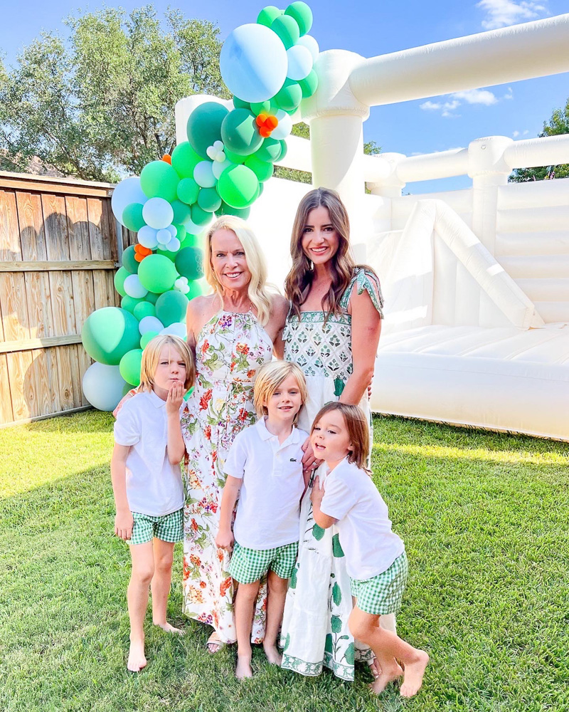 two women and three little boys standing in front of bounce house with balloon garland