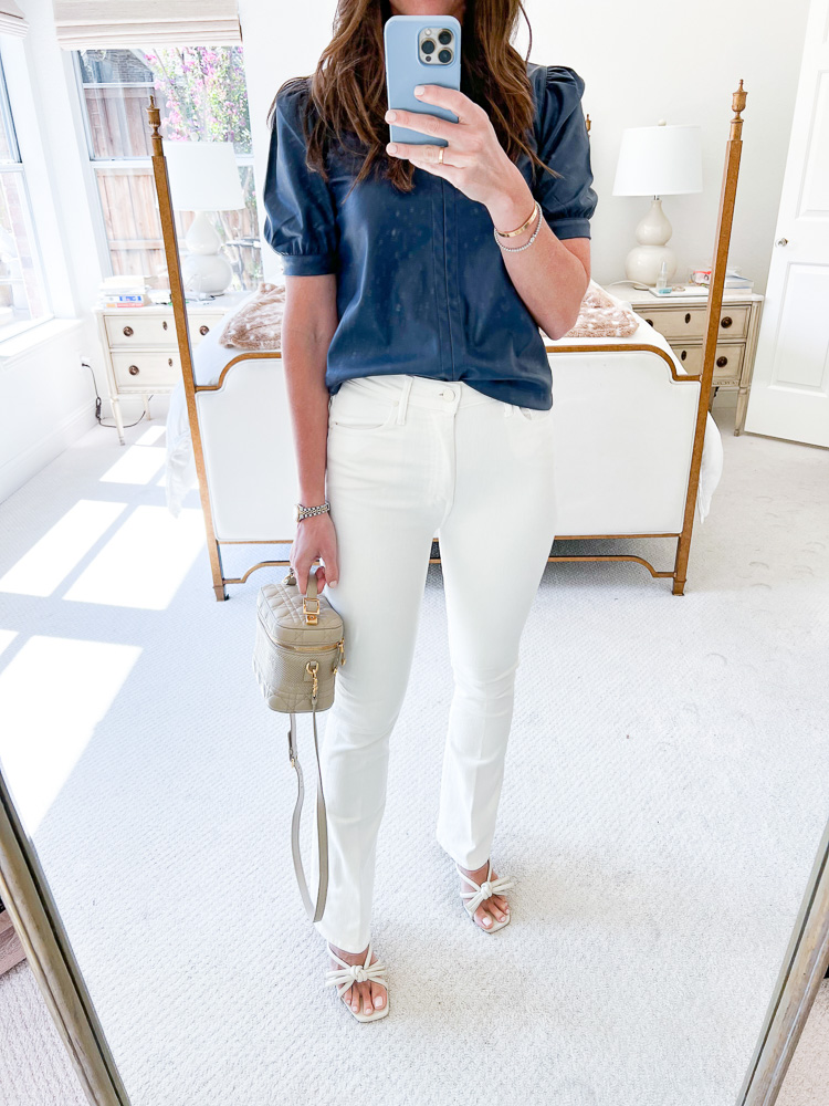 woman in blue leather top white jeans in front of bed
