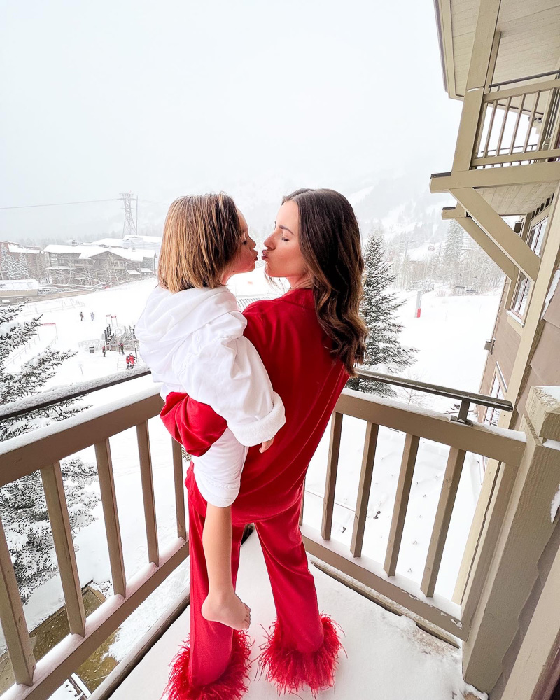 mom in feather pajamas with toddler boy in bathrobe standing on patio in the snow