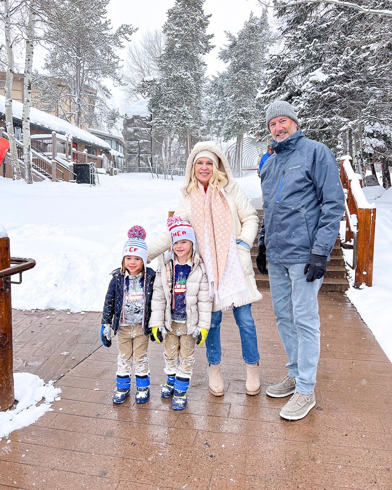grandparents with two toddler boys in snow gear standing in the snow