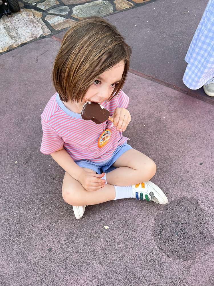 little boy sitting eaitng mickey ice cream bar