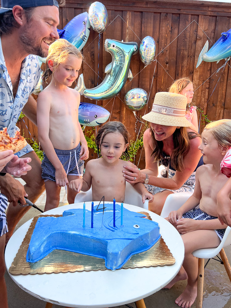 family singing happy birthday to little brother with shark cake