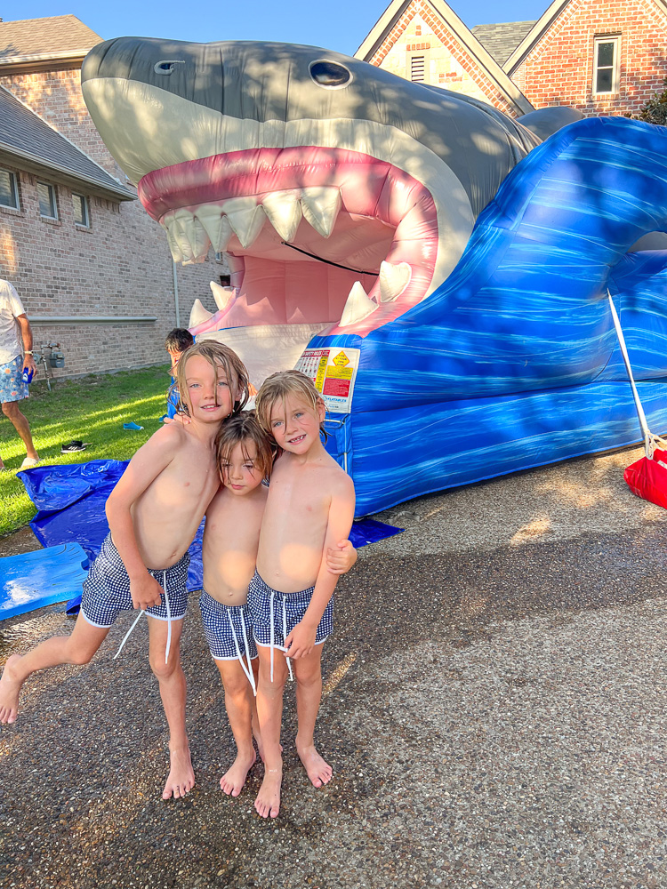 three little boys standing in front of shark slip and slide