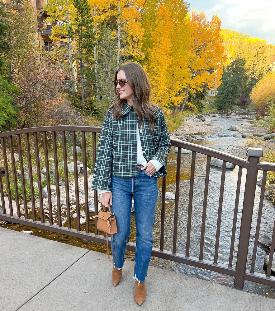 woman in plaid jacket and jeans standing on bridge over river vail