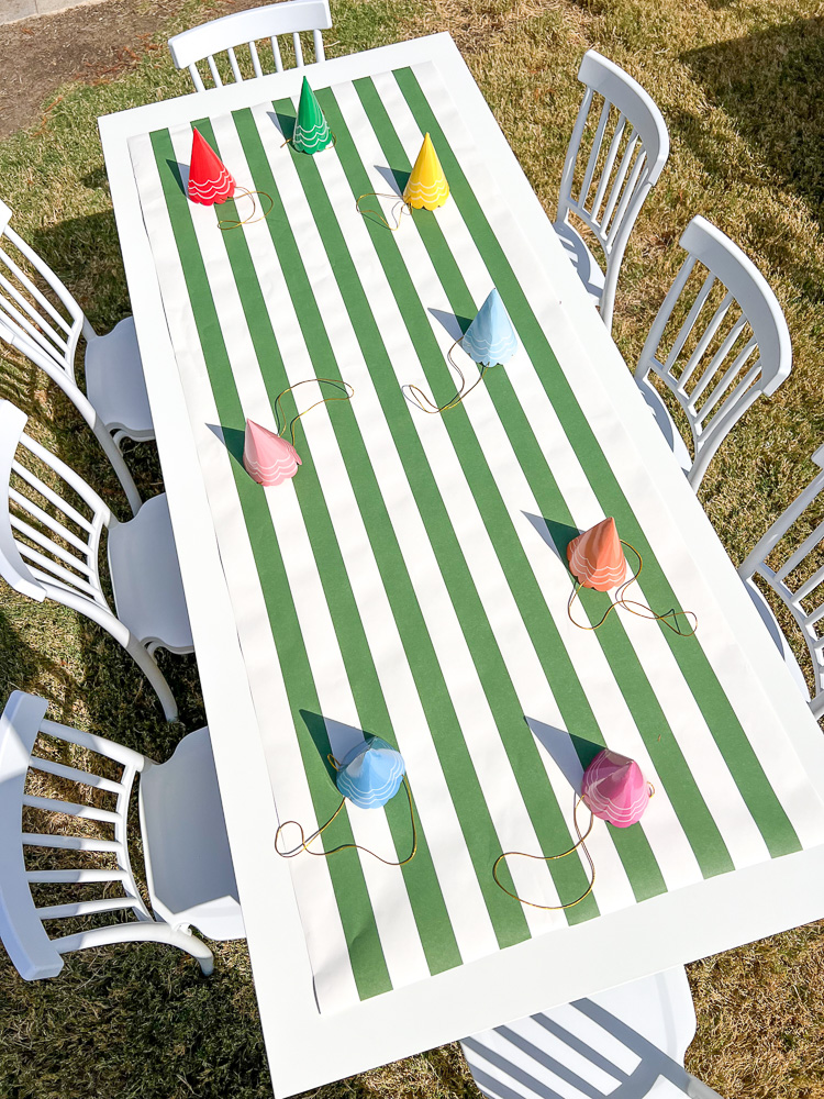 above view of party table with green and white runner and colorful party hats