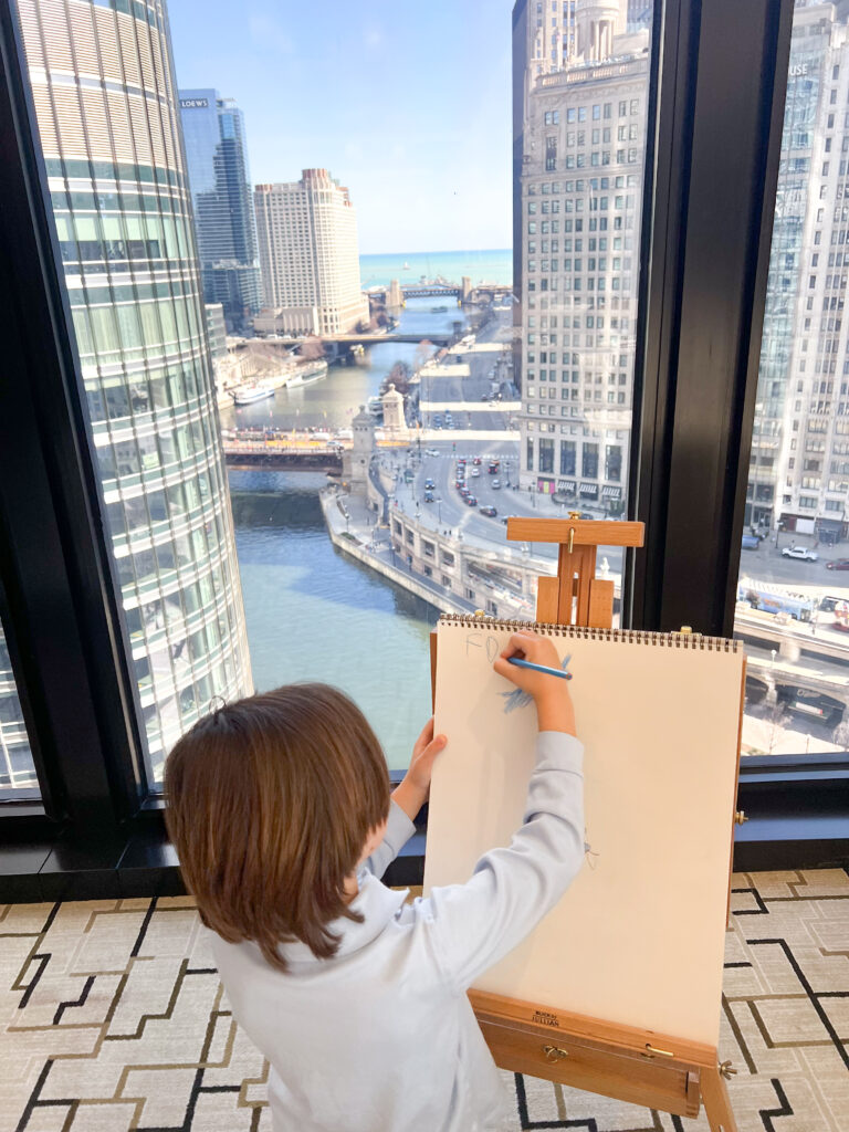 little boy drawing on an easel overlooking downtown chicago
