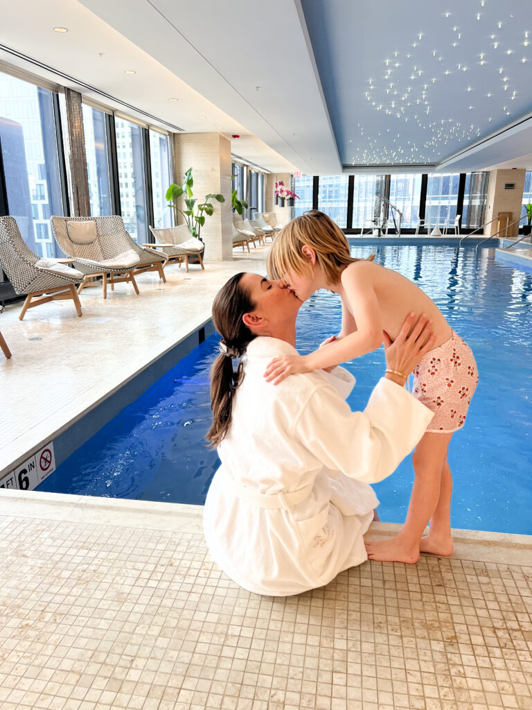 mom kissing little boy at the edge of indoor swimming pool